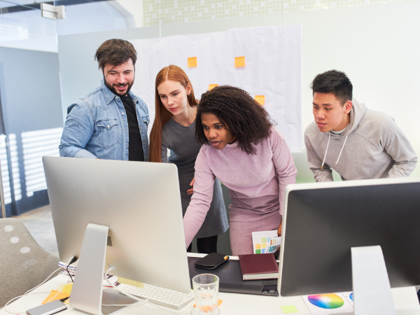 Four individuals standing around two computer monitors