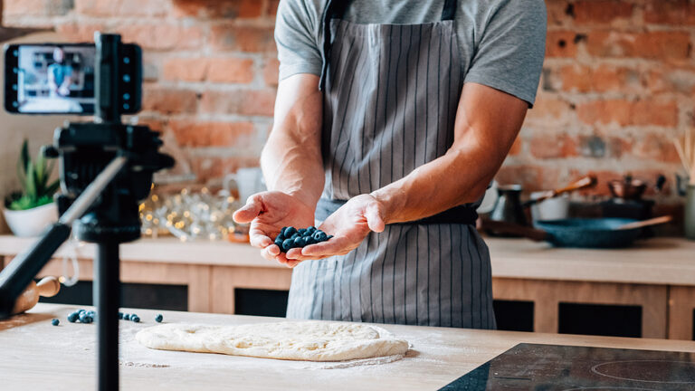 Male chef holding blueberries, shooting video using camera on tripod.