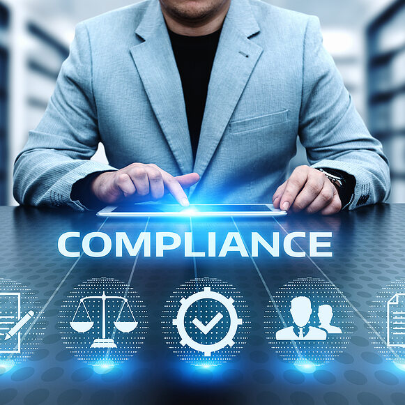 A business professional sits at a desk and uses a tablet while the word COMPLIANCE and related icons float in the foreground.