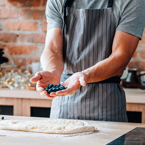 Male chef holding blueberries, shooting video using camera on tripod.